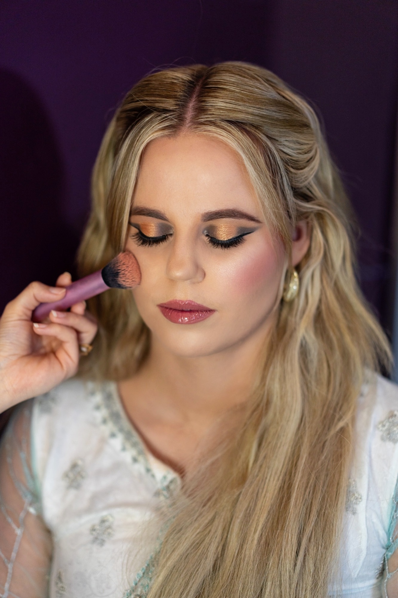 Bruidsmake-up met gouden oogschaduw en blush, aangebracht met een kwast